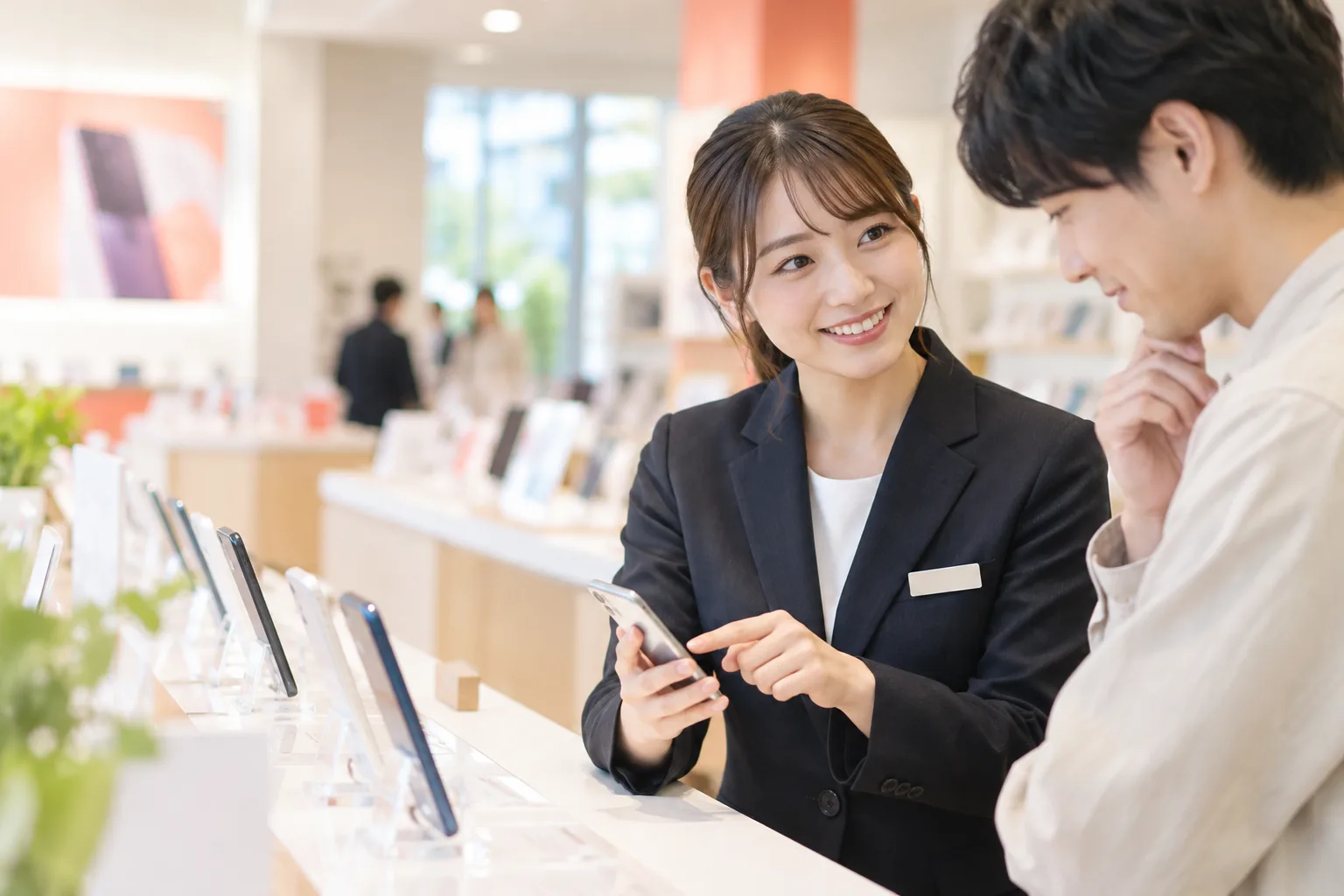 店頭で携帯販売スタッフがお客様にスマートフォンを案内する様子